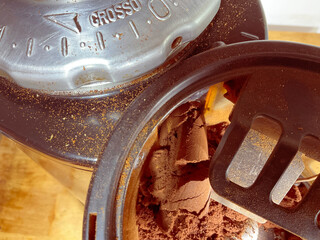 Closeup of a commercial coffee bean grinder in use, with a thick flow of ground coffee exiting the...