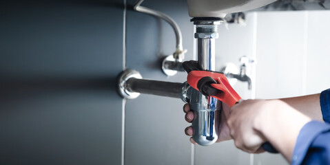 Plumber uses wrench to repair water pipe under sink There is maintenance to fix the water leak in the bathroom.with red wrench, plumbing install concept.