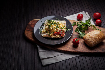 A rustic breakfast scene featuring scrambled eggs with herbs on toasted bread, garnished with tomatoes and parsley. Fresh tomatoes and a roll of bread complete the cozy, homemade setup.