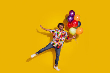 Full body photo of attractive young man hold air balloons dance funky dressed stylish colorful clothes isolated on yellow color background