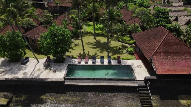 Aerial Drone Footage of Tropical Beachside Resort with Pool and Palm Trees.