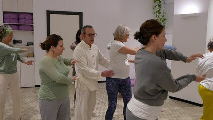 A group of senior women practices mindful movements during a yoga session, led by their instructor. Concept of mindfulness, physical health, and movement for seniors.