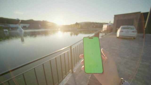 View on hands holding vertically phone with green screen moving around. On background beautiful lake. Nature. Typing on smartphone