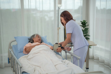 Asian nurse with tonometer measuring woman patient's blood pressure at hospital