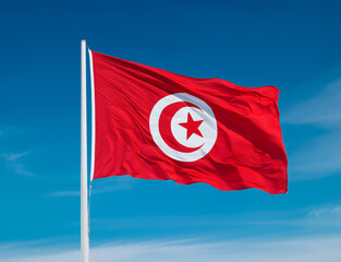 Tunisia flag waving in the wind against a blue sky background