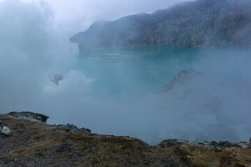 A mysterious and surreal landscape featuring a stunning, turquoise lake surrounded by misty vapors, creating a sense of awe and wonder