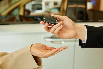 Close up on hand of auto dealer giving smart key to female client renting or buying vehicle at car rental office or dealership center, copy space