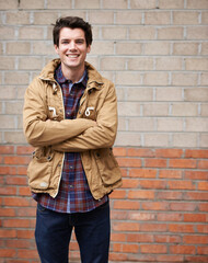 Obraz premium Happy, man and arms crossed for fashion on brick wall with style, clothes and outfit as web designer In New York. Male person, employee and outdoor with smile, confidence and pride for career growth
