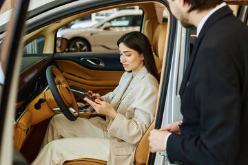 Young fashionable woman at drivers seat reading about car performance using digital tablet while...