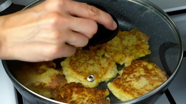 Potatoes pancakes, draniki cooking in frying pan on gas oven on kitchen at home. Preparing fresh dish. Cuisine, culinary, recipe. Traditional Russian food on lunch dinner fry on vegetable oil.