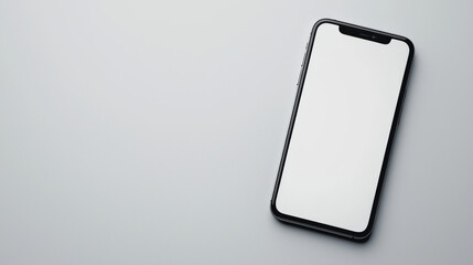 A black smartphone lies on a plain white surface with its blank screen.