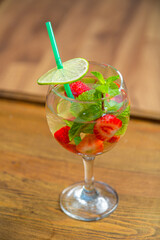 Glass with fruit cocktail strawberry mint lime with ice on wooden table