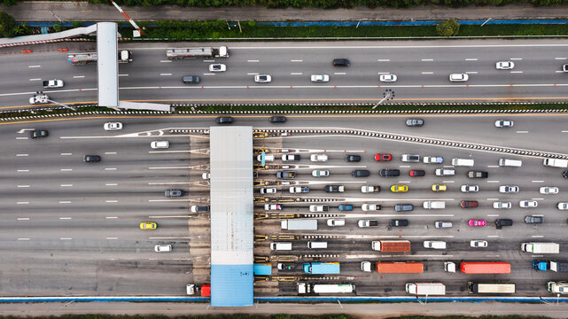 Aerial view of a bustling city expressway toll gate, featuring multiple lanes filled with vehicles waiting in line for fee payment.