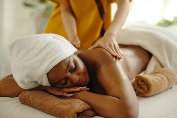 Woman enjoying relaxing massage at spa resort, lying on table with towel-covered head, receiving...