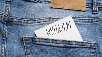 White card with a handwritten inscription "Wynajem", inserted into the pocket of blue pants jeasnow (selective focus), translation: Hire