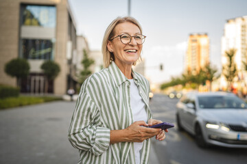 Fototapeta premium Happy mature woman stand and use mobile phone on the street
