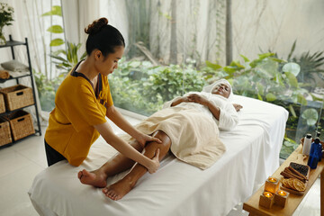 Woman providing professional massage therapy to customer lying on treatment table with towel