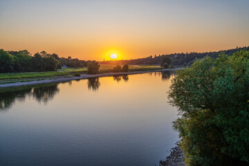 Obraz premium Sunset on river. Yellow disk of sun is sinking. river at sunset. People sitting on bank of the river Elba. Dresden.