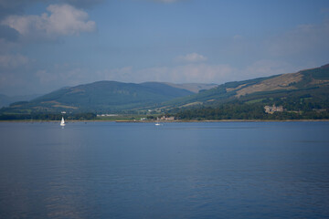 A tranquil scene with a sailboat on calm water, surrounded by mountains and fluffy clouds. A peaceful figure navigates another boat, showcasing serenity and harmony with nature.