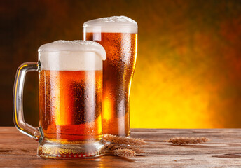 Glass of beer and mug of beer with wheat ears are on wooden table.