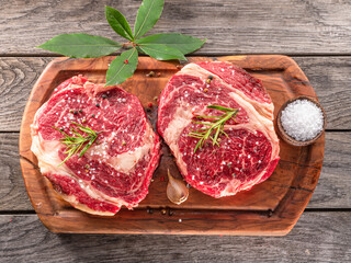 Raw beef steaks with herbs and spices ready for cooking are on wooden board.