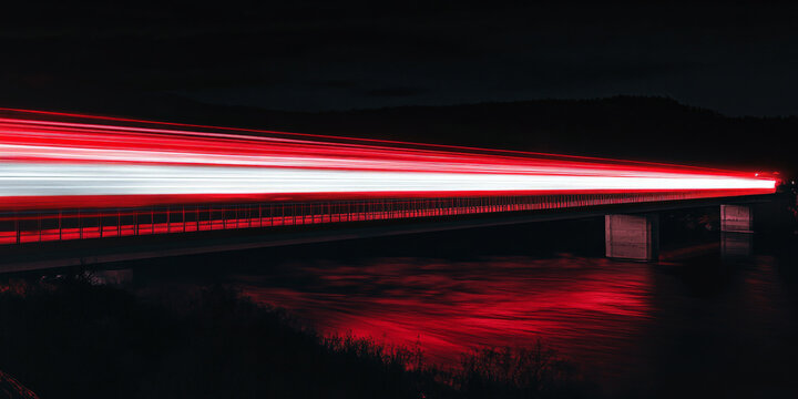 Red and white light trails flowing in parallel lines across a bridge at night, contrasting sharply with the dark sky and water below.