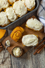 Freshly baked pumpkin cinnamon rolls or cinnabon with cream cheese on a rustic wooden table. Homemade seasonal autumn homemade pastry.