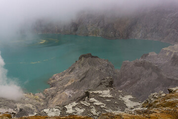 A breathtaking view of a vibrant turquoise lake surrounded by a dramatic, rocky landscape, shrouded in mist