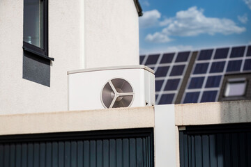 Wärmepumpe auf einem Garagendach eines Neubaugebiets, im Hintergrund sind Solarpanele auf...