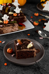 Halloween chocolate cake. Dirty cake with chocolate cream, decorated with worms, skulls, ghosts, pumpkins and sugar sprinkles on a dark background.