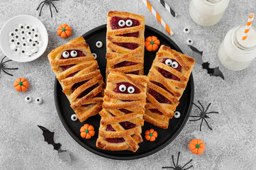 Halloween mummies pies with cherry filling and sugar eyes on a gray concrete background. Funny food...