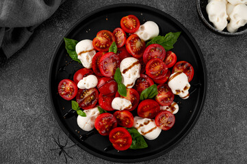 Halloween food. Caprese salad with mozzarella cheese skulls, basil and balsamic dressing on a black plate on a dark background. Funny food idea.