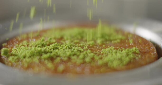 Traditional Turkish kunefe close-up. Chef sprinkle shredded pistachios on kunefa or kanafeh in a copper plate