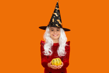 Halloween pumpkin in hand of witch girl. Halloween witch girl isolated on orange. Pumpkin on Halloween. Witch All Hallows costume of girl. October 31 pumpkin. Costume party. Enchanted pumpkin