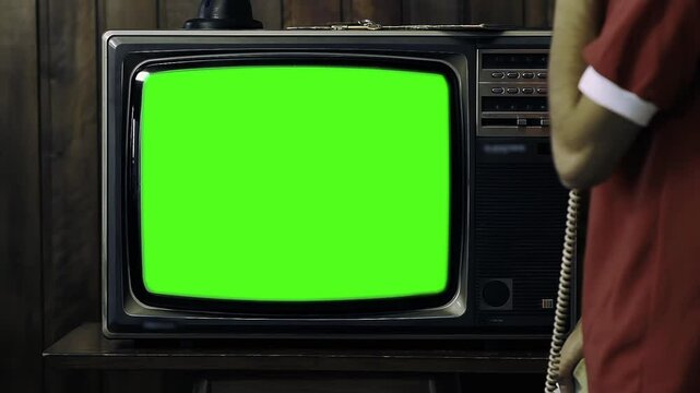 Man Holding 80s Phone While Turning On Old TV with Green Screen in a Dimly Lit Room - You Can Replace Green Screen with the Footage or Picture You Want with 'Keying' Effect (Check Out Tutorials) - 4K