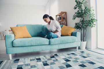 Full body portrait of nice young woman touch hurt stomach sofa wear shirt modern interior flat indoors