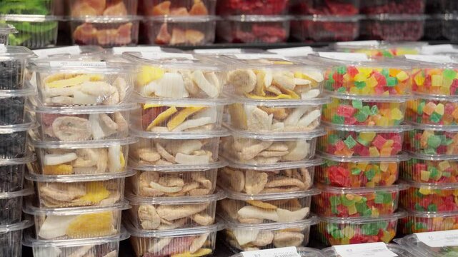 Food retailer is arranging plastic trays of dried fruits and nuts on shelf. Trays are arranged in rows, with different types of fruit and nuts in each row