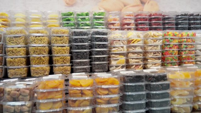 Food retailer is arranging plastic trays of dried fruits and nuts on shelf. Trays are arranged in rows, with different types of fruit and nuts in each row