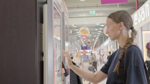 Young woman, customer, interacting with digital order kiosk in restaurant, browsing menu and choosing desired items in fast food restaurant, fast food.