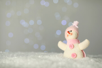 Cute decorative snowman on artificial snow against blurred lights. Space for text