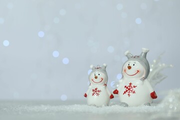 Cute decorative snowmen on artificial snow against blurred lights. Space for text