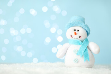 Cute decorative snowman on artificial snow against blurred lights. Space for text