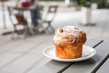 A cruffin on the plate on the table of a city cafe or bakery terrace
