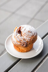 A cruffin on the plate on the table of a city cafe or bakery terrace