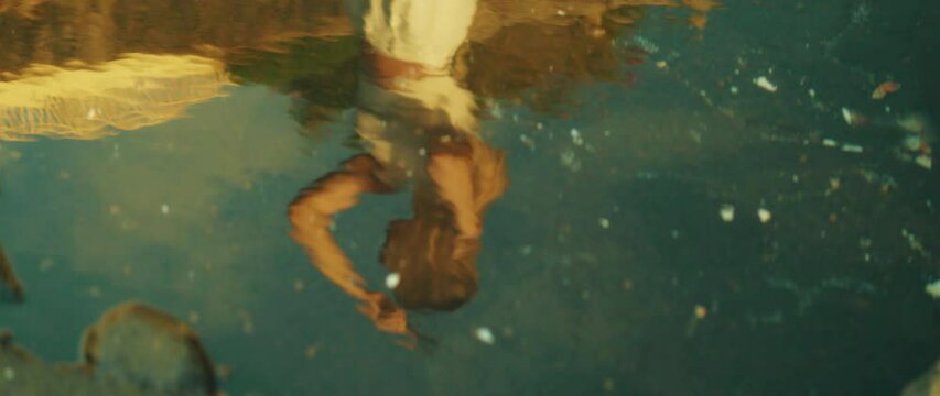 Reflection of a woman in water, her hand touching her head. Adult girl combing her hair on beach by the ocean.