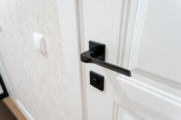 This image shows a close up of a white door featuring a sleek black door handle