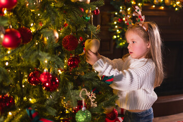 Merry Christmas Xmas holiday. Little girl decorating Christmas tree on Christmas eve at home. Young...