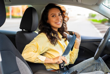 Pretty woman sitting on drivers seat and fastening seat belt before start driving and smiling at camera. Car safety concept