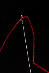 Macro of a red thread through the eye of a needle