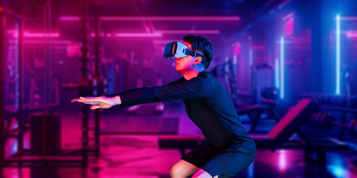 Asian man wearing VR glass while exercising at futuristic gym with glowing vibrant color. Male model using augmented reality technology for analysis data. Technology innovation concept. Ingenuity.
